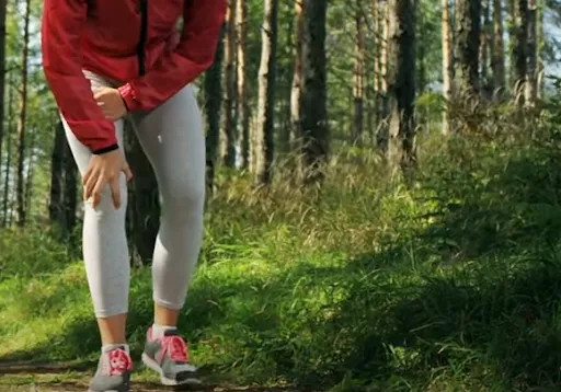 Person holding knee due to joint pain while walking in a forest, showing symptoms of knee injury, arthritis, or joint discomfort during outdoor activity